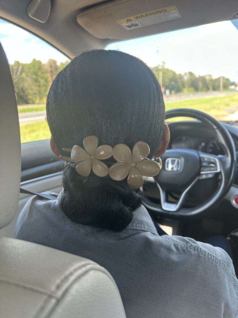 Low sleek bun on natural hair secured with a flower-shaped clip